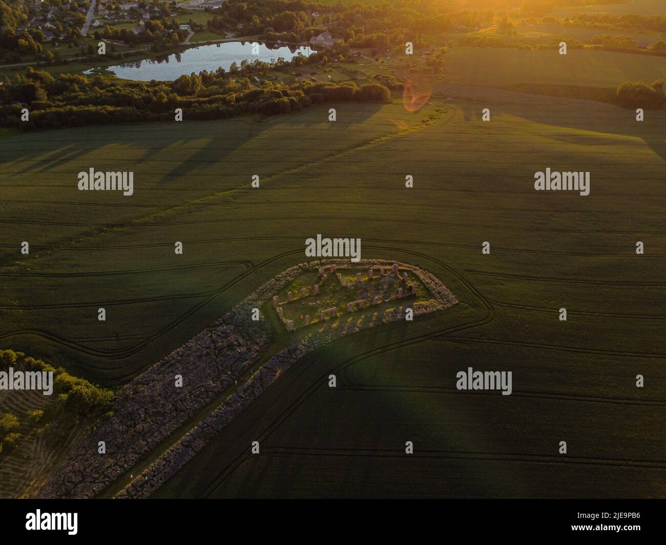 Luftaufnahme mit wunderschönem Getreidefeld bei Sonnenuntergang mit einem riesigen Steinhaus in der Mitte des Feldes. Das Gebäude ähnelt stonehenge. Smiltene ston Stockfoto