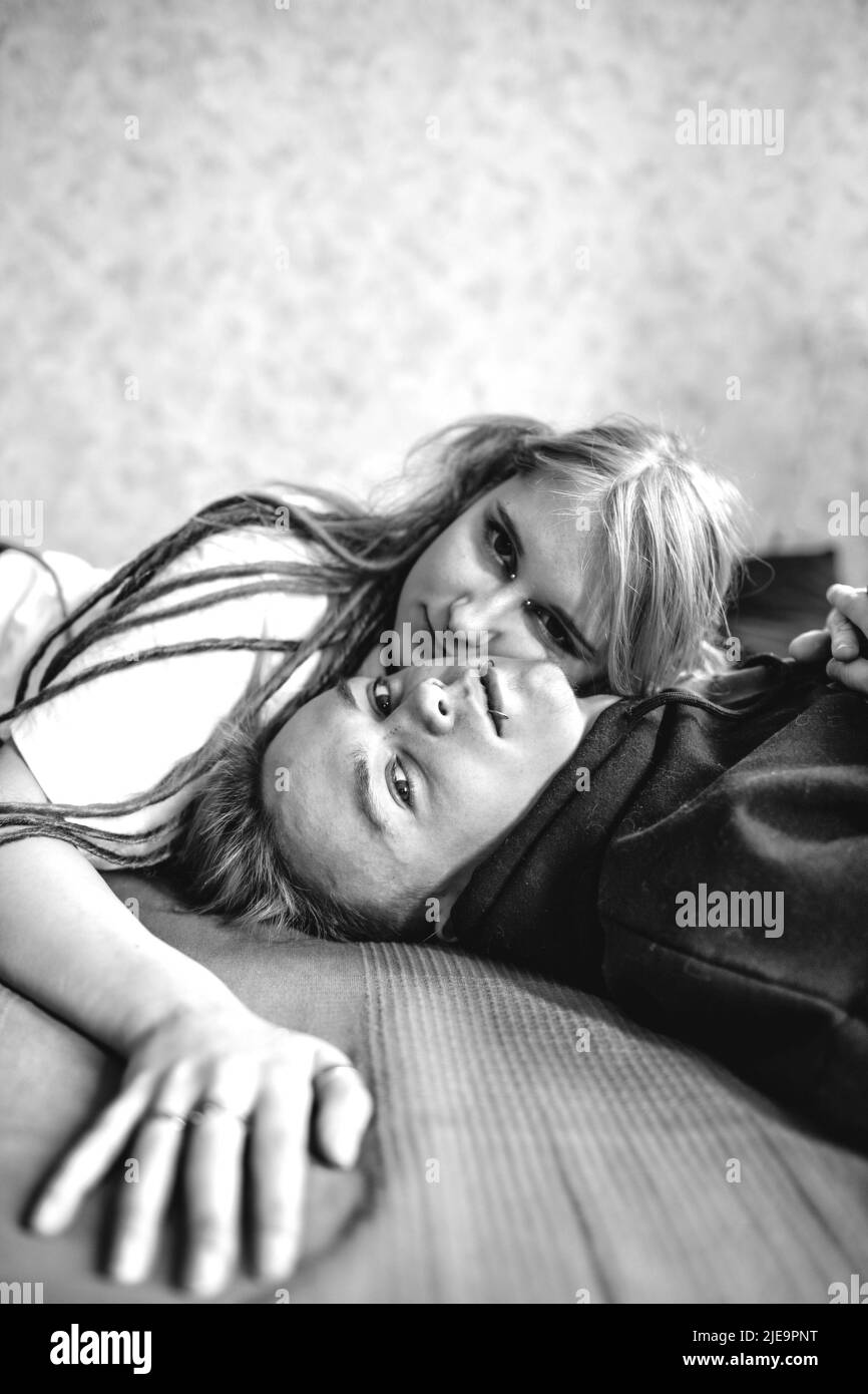 Porträt eines jungen tätowierten Punk-Paares eines Mädchens und eines Mannes mit langgefärbten Haaren geflochten, auf einem großen Bett liegend. Stylische, moderne Jugend Stockfoto