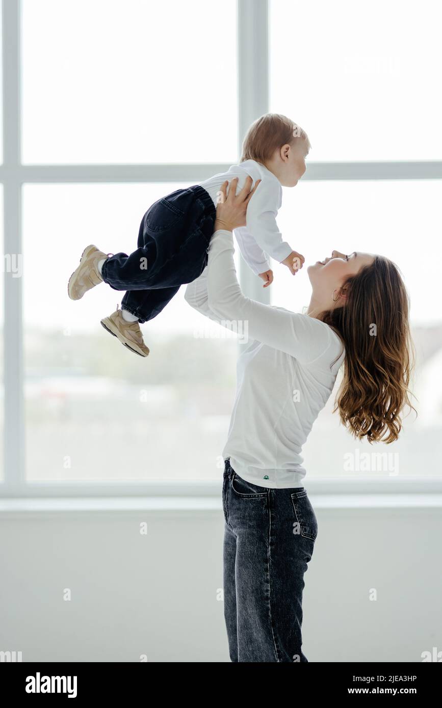 Mama liebt es. Junge Mutter hält Kleinkind Sohn auf den Händen, kuscheln mit Kind Junge, stehen in der Nähe Fenster drinnen, freien Raum. Stockfoto