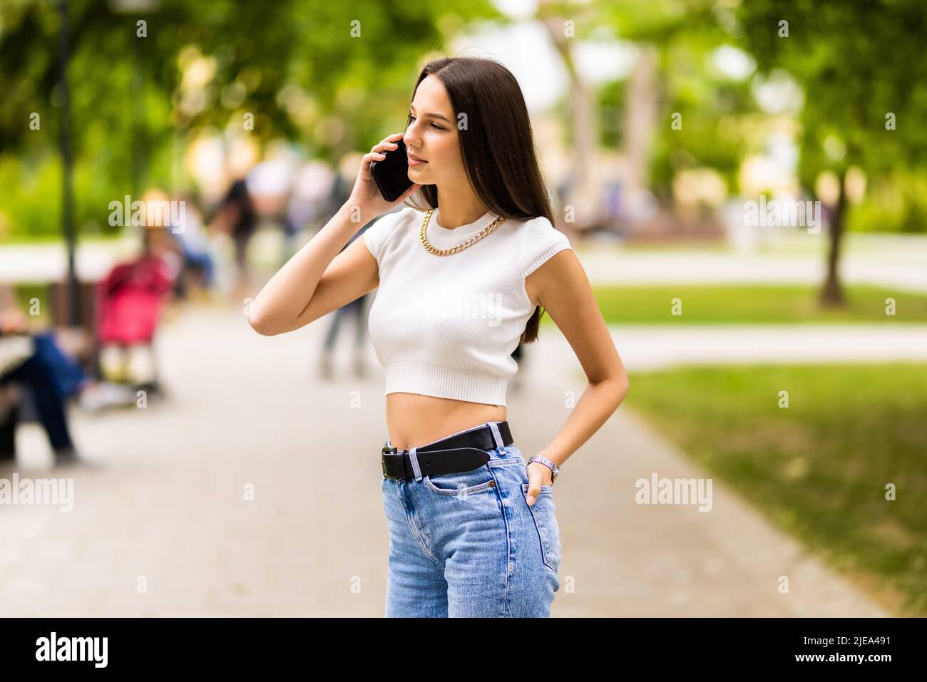 Porträt einer jungen attraktiven dunkelhaarigen Frau, die im Sommer im grünen Park auf dem Mobiltelefon spricht. Stockfoto