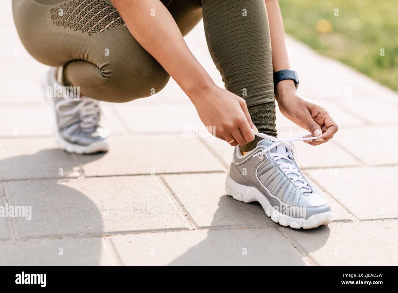 Die schwarze Millenial-Sportlerin schnürt ihre Schuhe, während sie im Park joggt, aus der Nähe der Beine Stockfoto