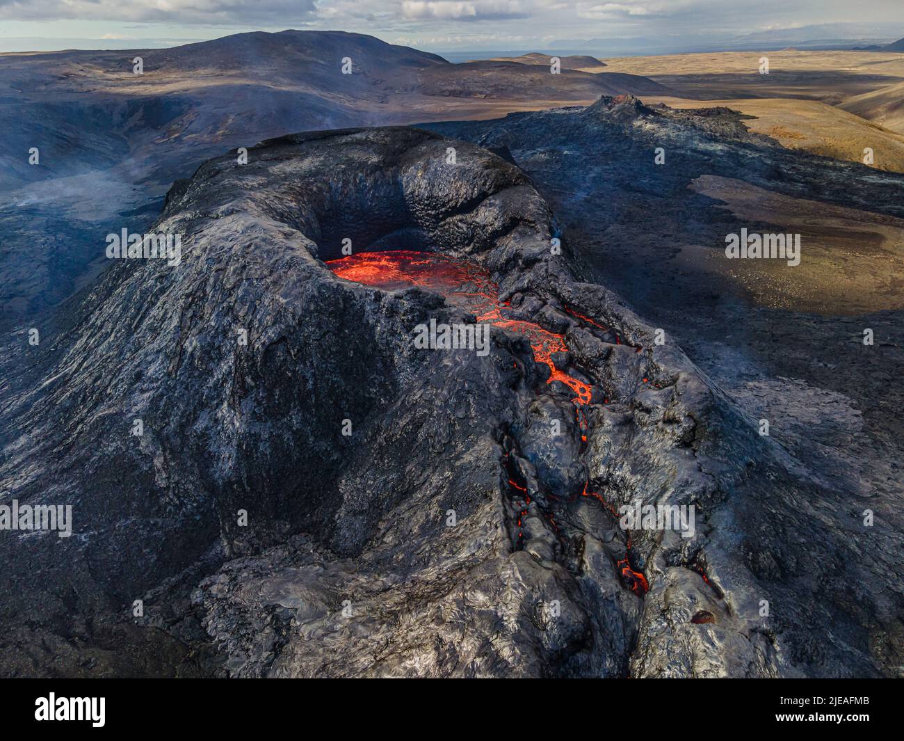 Krater eines aktiven Vulkans mit Lavastrom. Landschaft auf der Halbinsel Reykjanes in Island. Rauch- und Dampfschwaden rund um den Krater. Brown Hills i Stockfoto