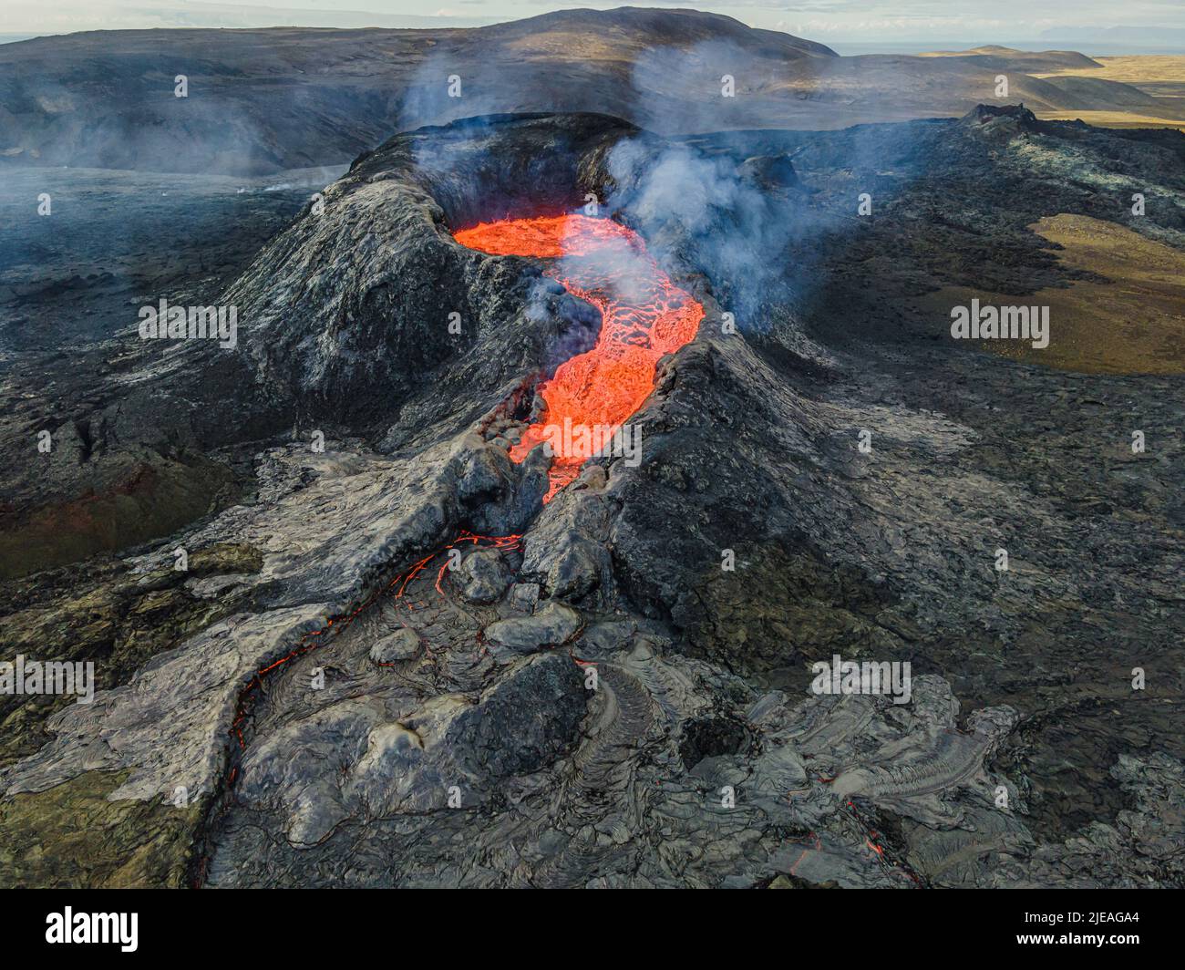 Vulkanlandschaft auf der isländischen Halbinsel Reykjanes. Blick auf den Krater von oben. Flüssige Lava fließt heraus. Dampf und Rauch in der Nähe des Krater. Stockfoto