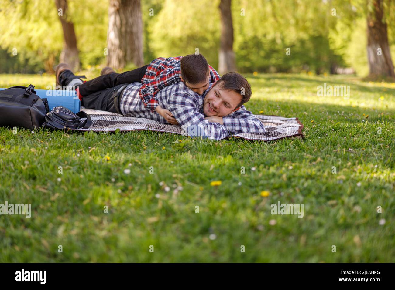 Glücklicher Vater, der sich im Park ausruhte, und kleiner Sohn, der auf dem Rücken des Vaters lag. Entspannung mit Kind. Stockfoto