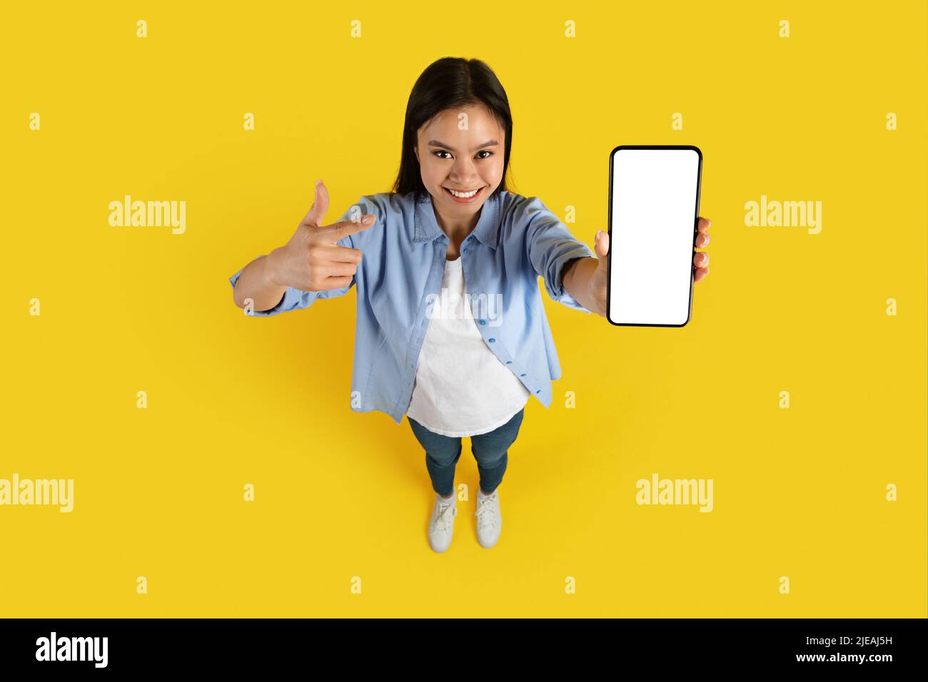 Fröhliche tausendjährige japanische Frau zeigen Finger auf Smartphone mit leerem Bildschirm, empfiehlt Website Stockfoto