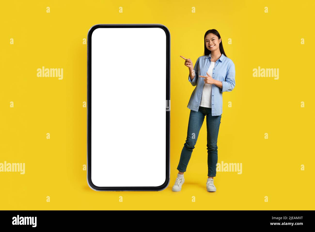 Soziale Netzwerke und Chat. Fröhliche junge asiatische Dame, die mit dem Finger auf ein riesiges Telefon mit leerem Bildschirm zeigt Stockfoto
