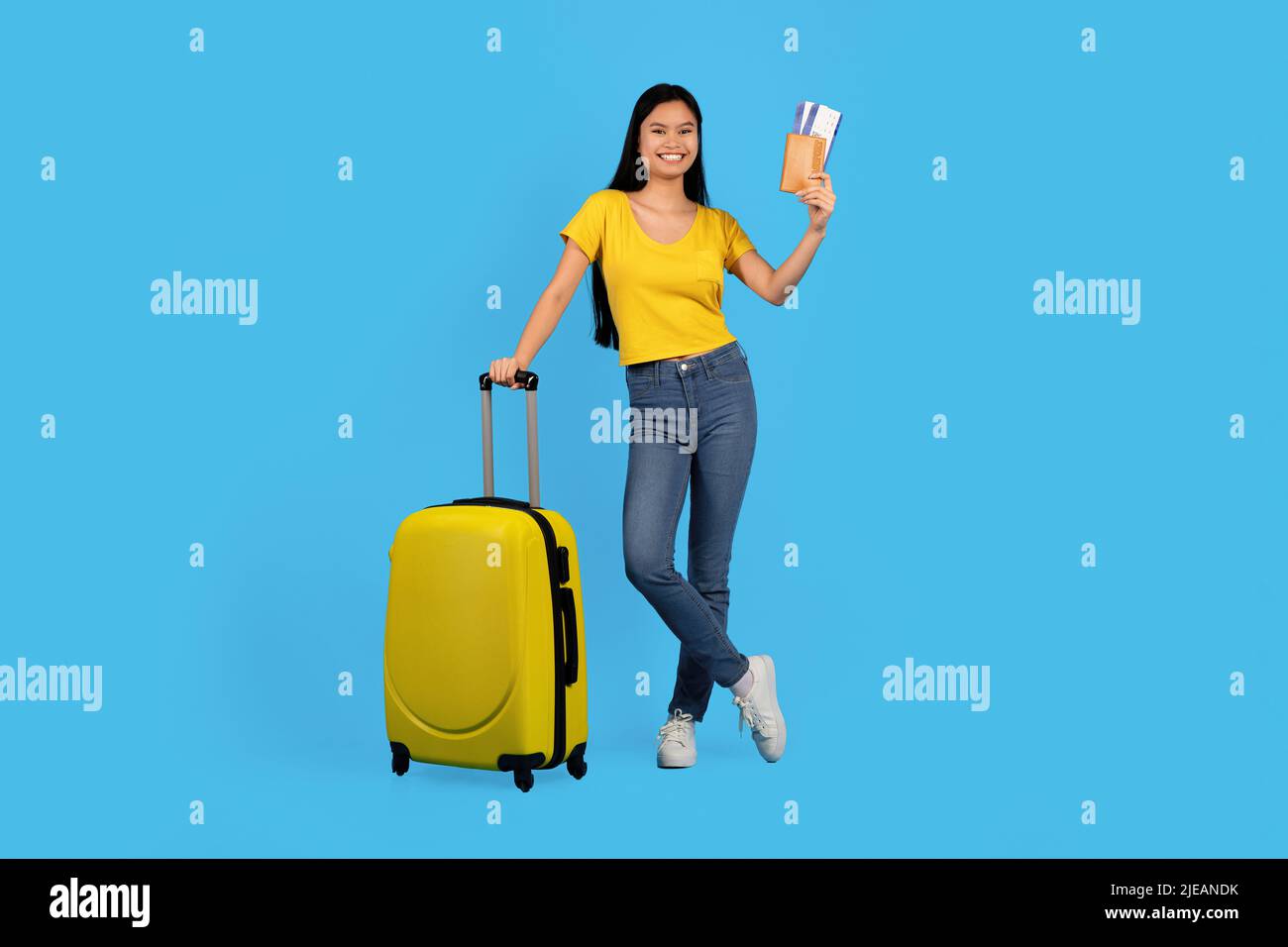 Happy hübsche junge chinesische Frau in gelben T-Shirt halten Pass und Flugtickets steht mit Koffer Stockfoto