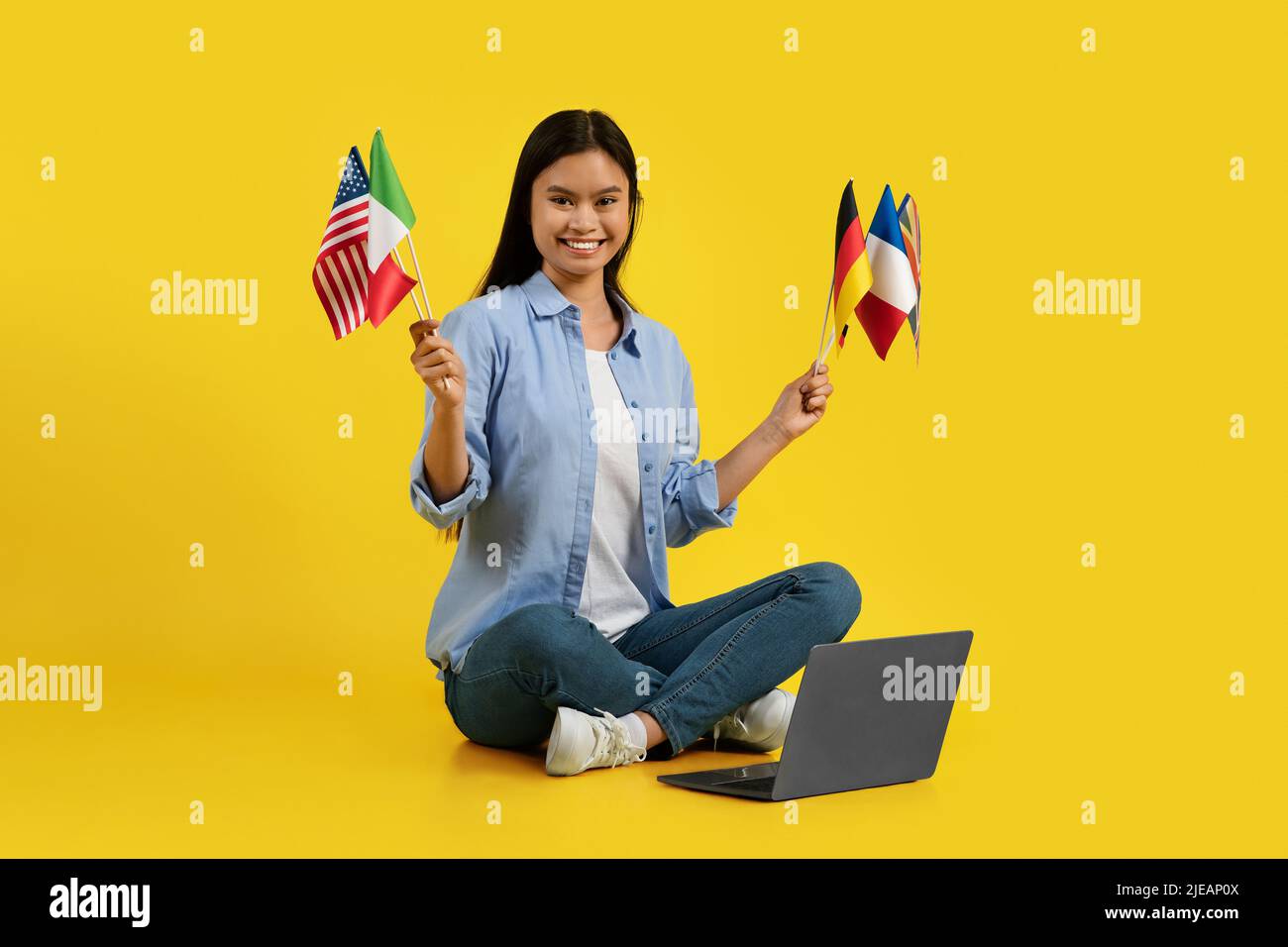 Frohes tausendjähriges koreanisches Lehrerin mit vielen verschiedenen Flaggen, die auf dem Boden mit einem Laptop sitzen Stockfoto