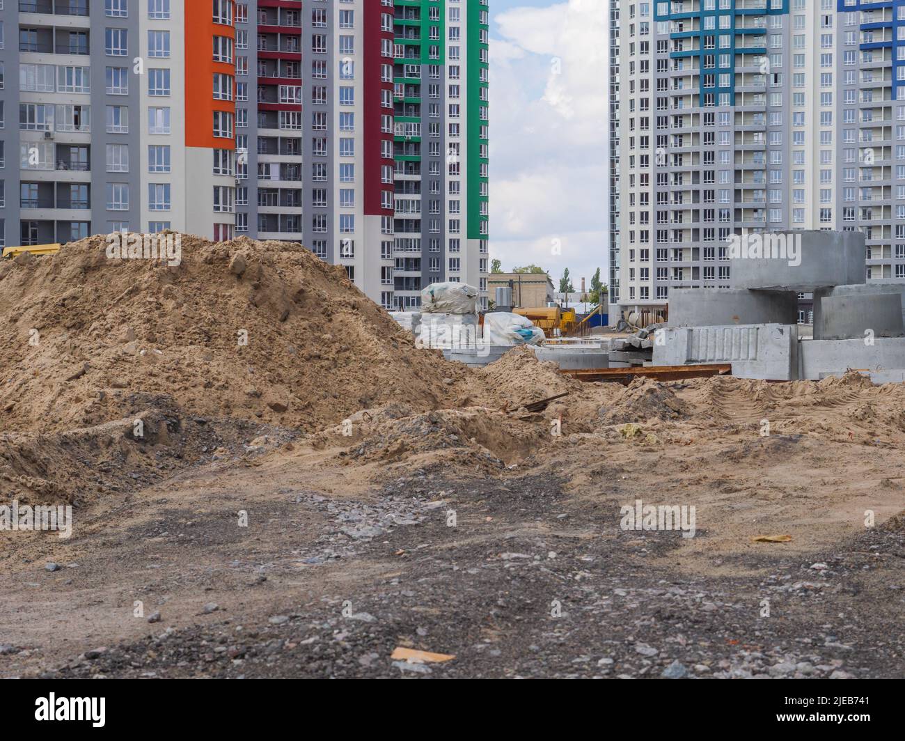 Eine Baustelle mit neuen Hochhäusern und Baumaschinen im Hintergrund und verschwommenen Sandhaufen, Betonringe im Vordergrund. Stockfoto