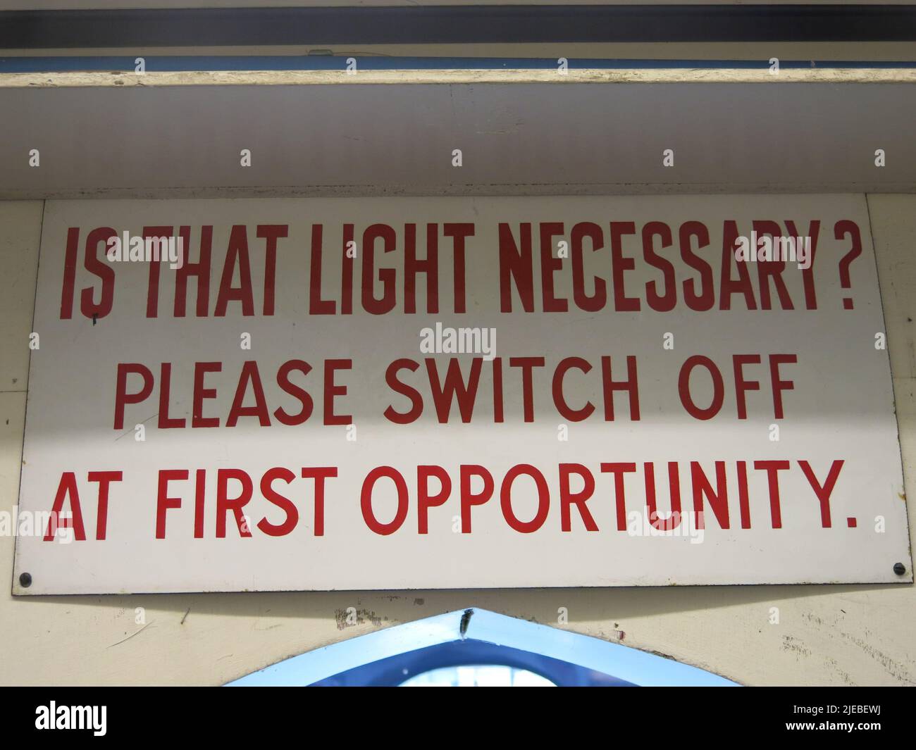 Altes Bahnschild, das eine moderne Botschaft zum Energiesparen vermittelt: 'Ist das Licht notwendig? Bitte bei der ersten Gelegenheit ausschalten.“ Stockfoto