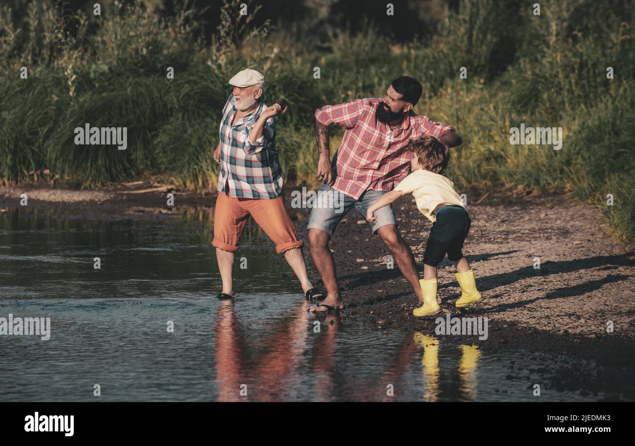Männliches Kind mit Vater und Großvater, die Steine auf dem Wasser überspringen. Mann in verschiedenen Altersgruppen. Stockfoto