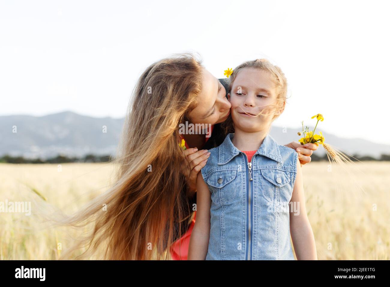 Porträt einer glücklichen jungen Mutter und ihrer schönen Tochter, die in einem Weizenfeld spielt und lacht. Freiheit Konzept.Mama küssen Tochter. Stockfoto