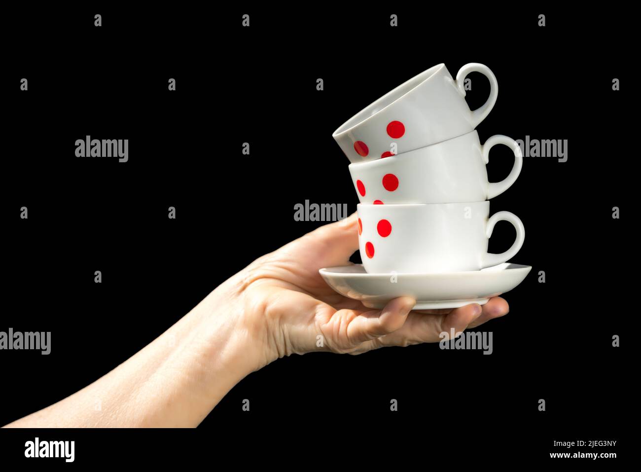 Kaffeetassen in roten Punkten stapeln sich in der Hand isoliert auf schwarzem Hintergrund. Stockfoto