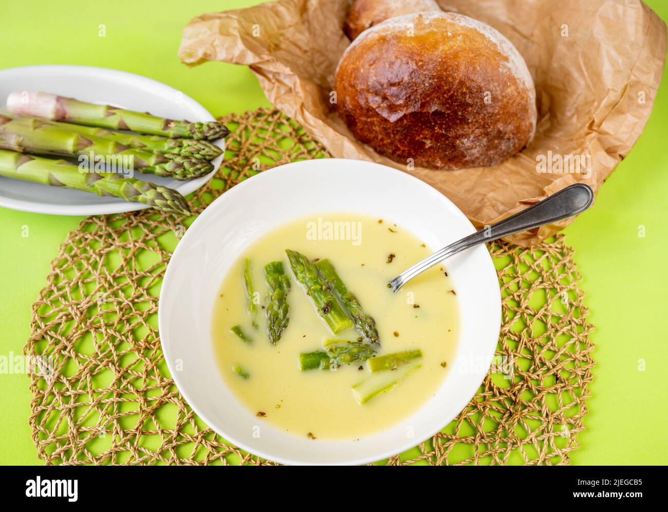 Spargelsuppe auf dem Teller, Brot auf Papier, roher Spargel auf dem Teller, Bambuskissen auf grünem Hintergrund, Nahaufnahme. Stockfoto
