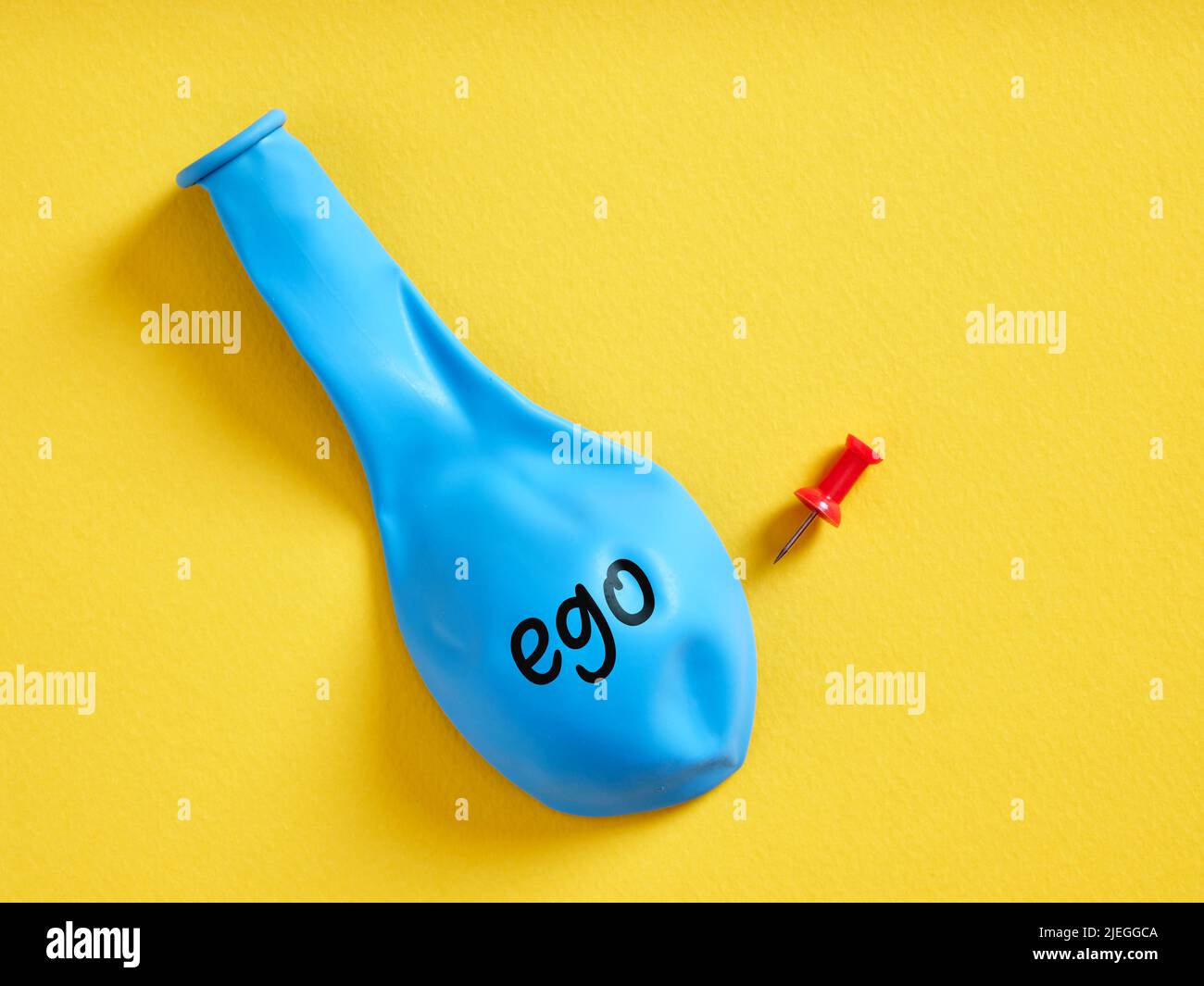 Entflammener blauer Ballon mit dem Wort Ego und einer Nadel. Egoismus oder Rückschritt des extremen Ego-Konzepts. Stockfoto