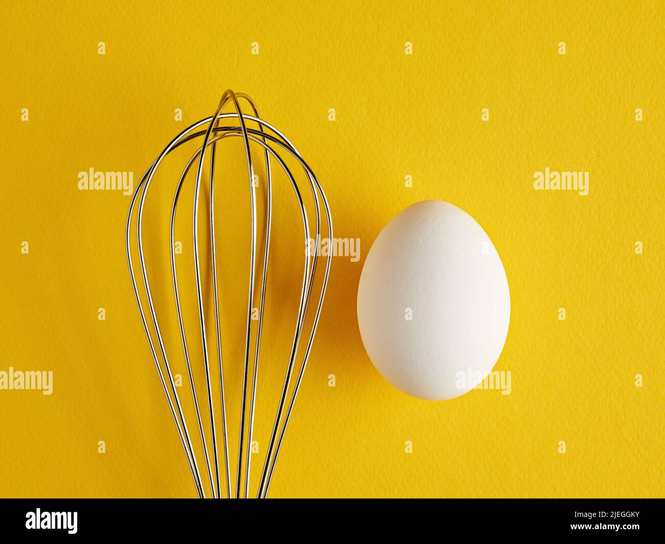 Ein Whisker und ein weißes Ei auf gelbem Hintergrund. Rührbesen zum Kochen von Eierquirlen. Stockfoto