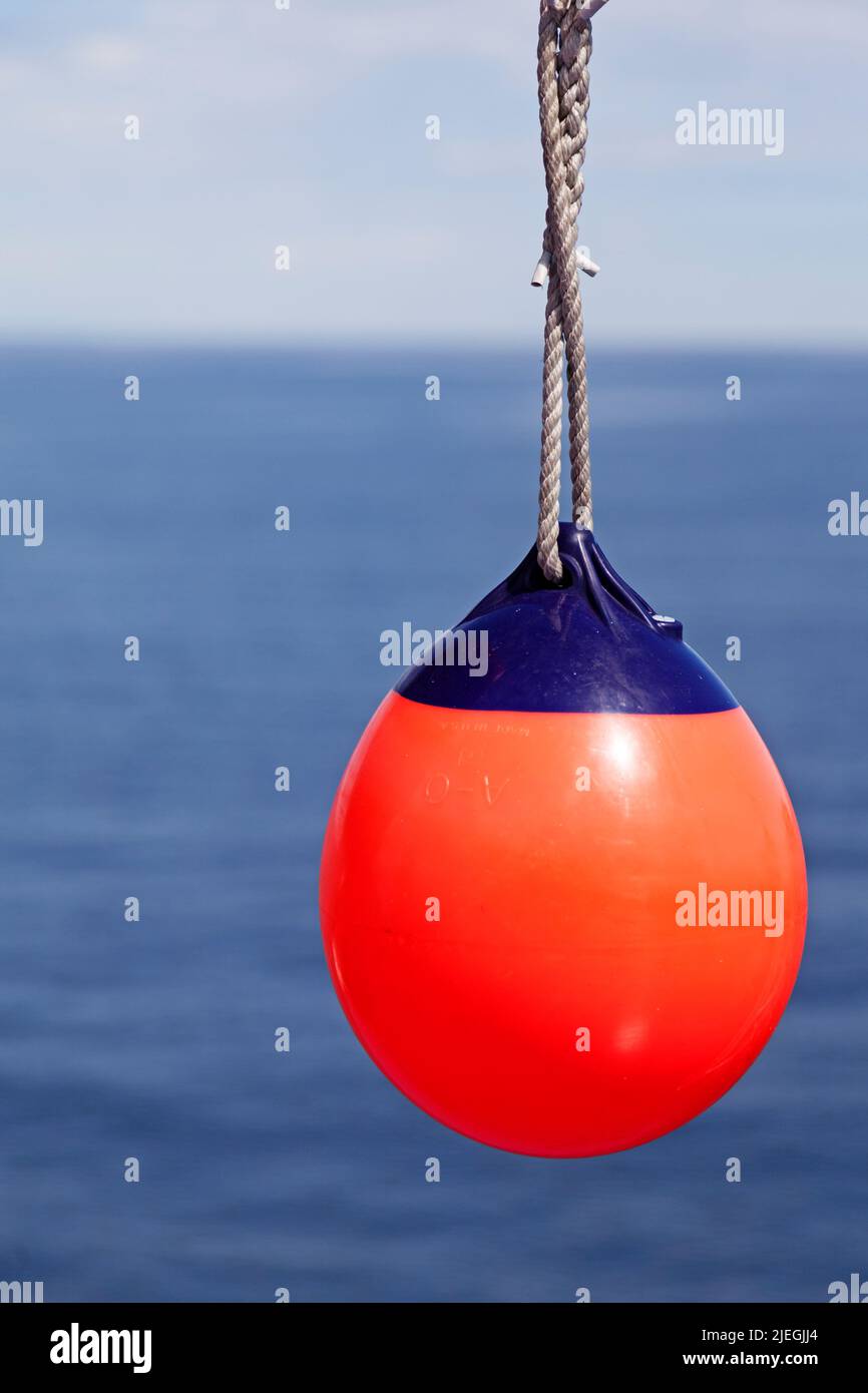 Rote Boje, die per Schiff in einem Seil hängt, mit dem Meer im Hintergrund Stockfoto