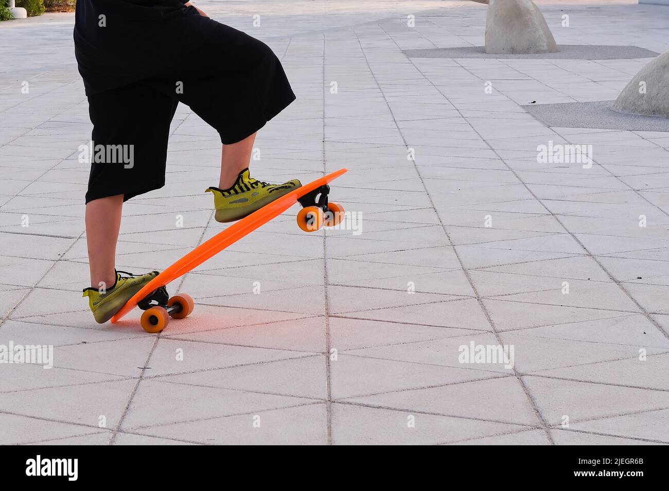 Ein Junge in breiten schwarzen Hosen und Sneakers reitet auf einer urbanen Straße trendige Skateboard Kreuzer. Beine des Schuljungen Skateboarding Stockfoto