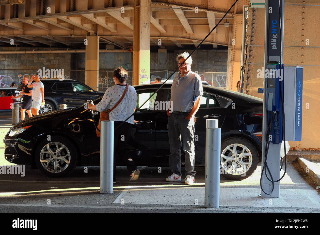 Leute, die ein seltenes Plug-NYC-Ladegerät für Elektrofahrzeuge am Straßenrand benutzen, um ihr Elektroauto in New York City aufzuladen. Das öffentliche EV-Netz ist .. (Siehe Info) Stockfoto