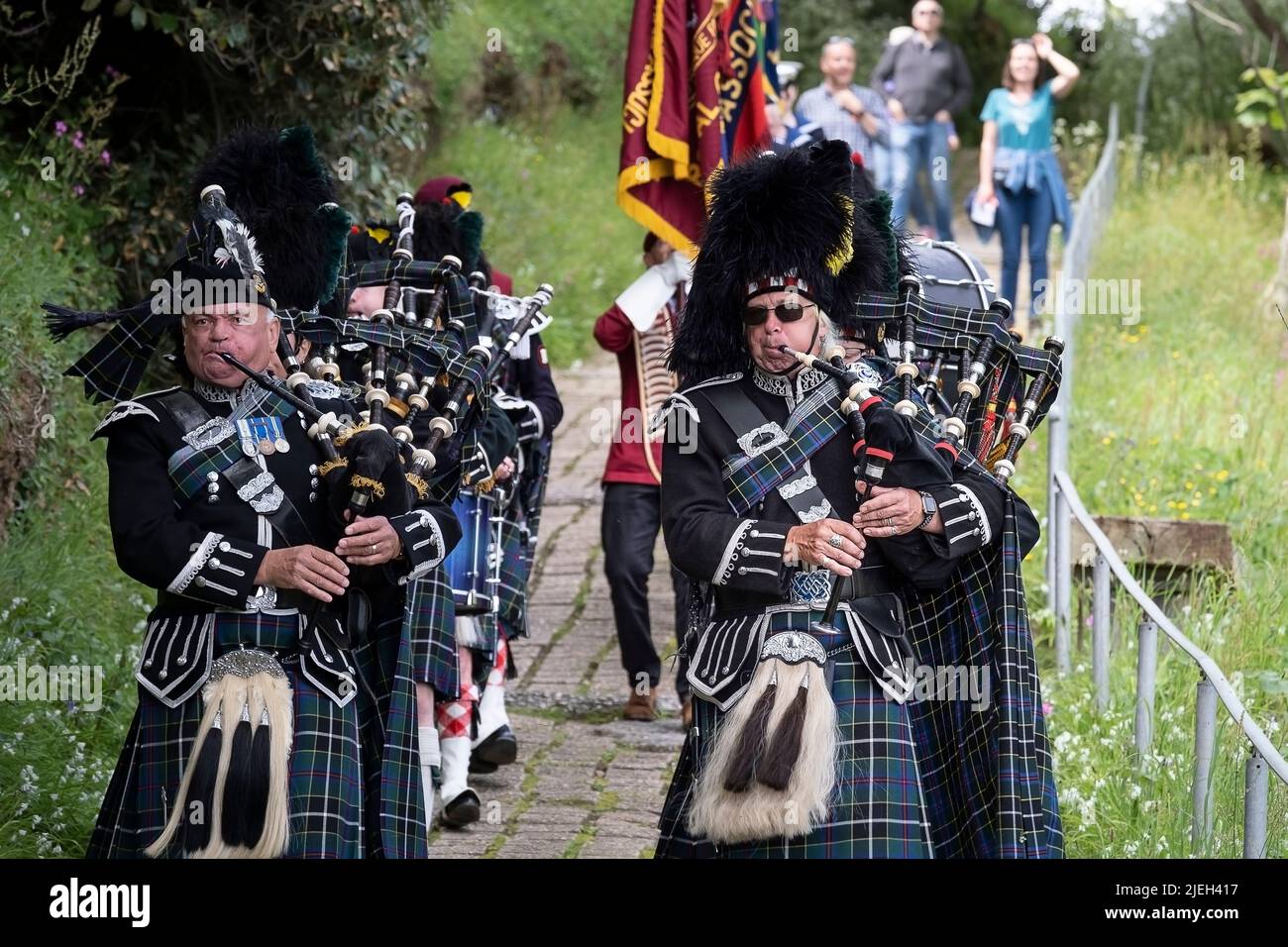 Kernow Pipe and Drums führt die Parade der Standards der Regimental Association nach Polgwidden Cove zur Wiederweihung der Gedenkstätten an die alliierte Ai an Stockfoto