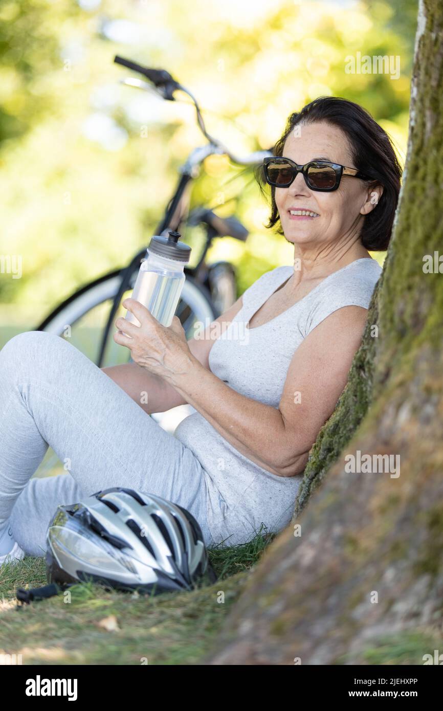 Ältere Radfahrerin ruht auf Baumstamm Stockfoto