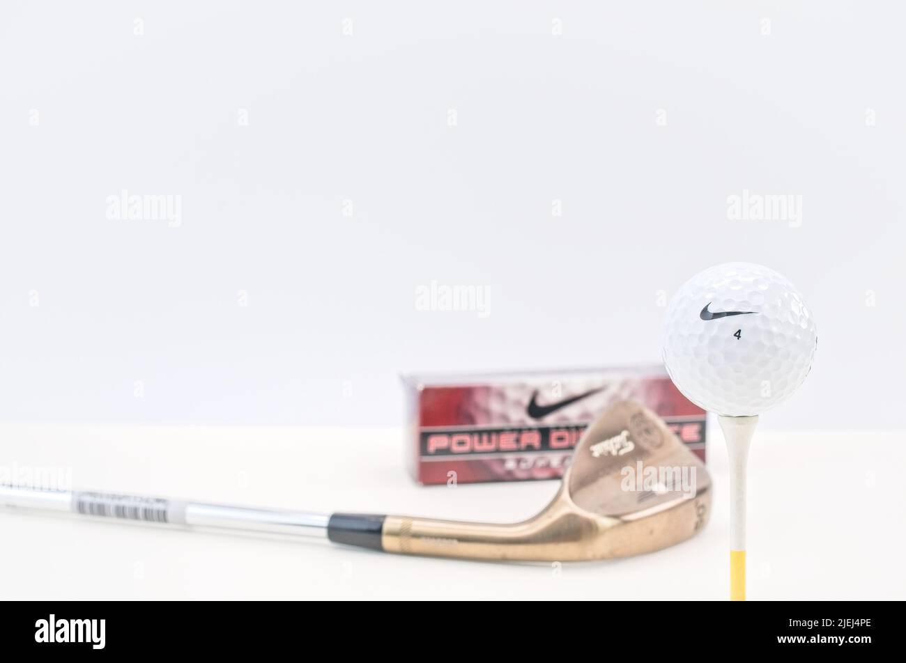 Golfball mit Box, Tee und Golfschläger auf einer hellen Oberfläche mit weißem Wandhintergrund Stockfoto