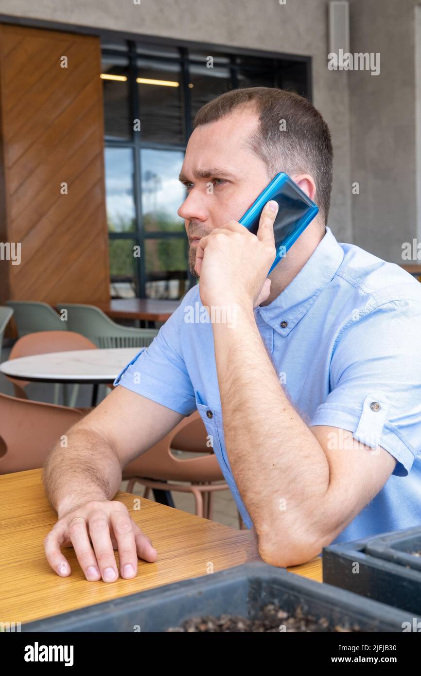 Ein arabischer Mann mittleren Alters mit Bart telefoniert in einem Café im Freien. Lächelnder Geschäftsmann im mittleren Alter, Freiberufler mit Mobiltelefon Stockfoto