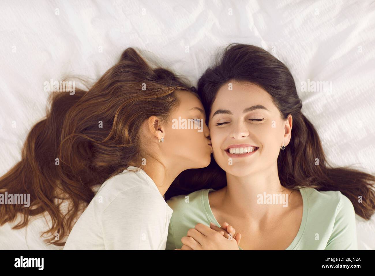 Ein glückliches, liebevolles Kind küsst ihre Mutter auf die Wange, als sie sie am Morgen aufweckt Stockfoto