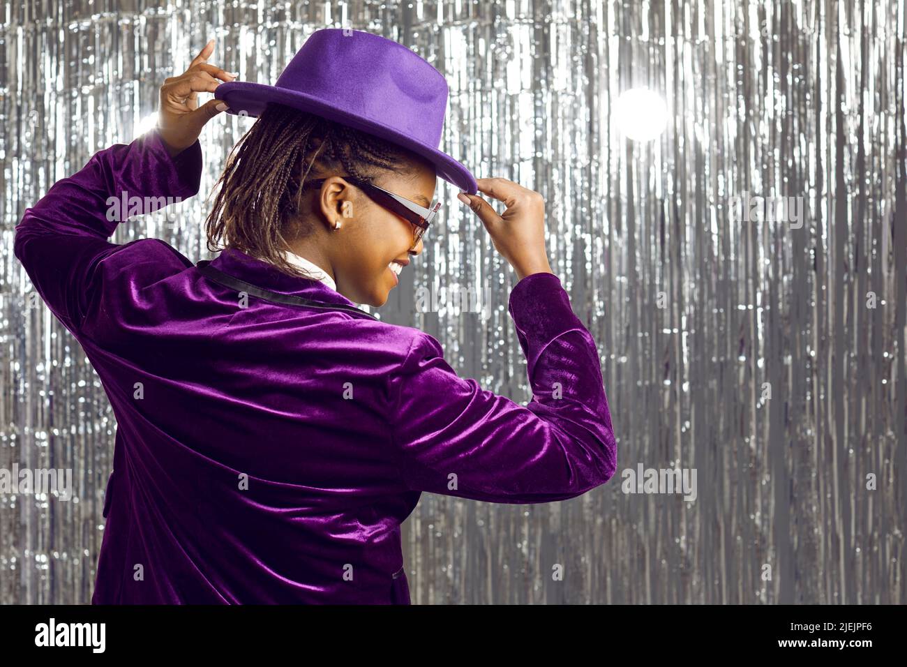 Glückliche junge afroamerikanische Frau in purpurem Hut, die sich auf der Disco-Nachtclub-Party amüsieren kann Stockfoto