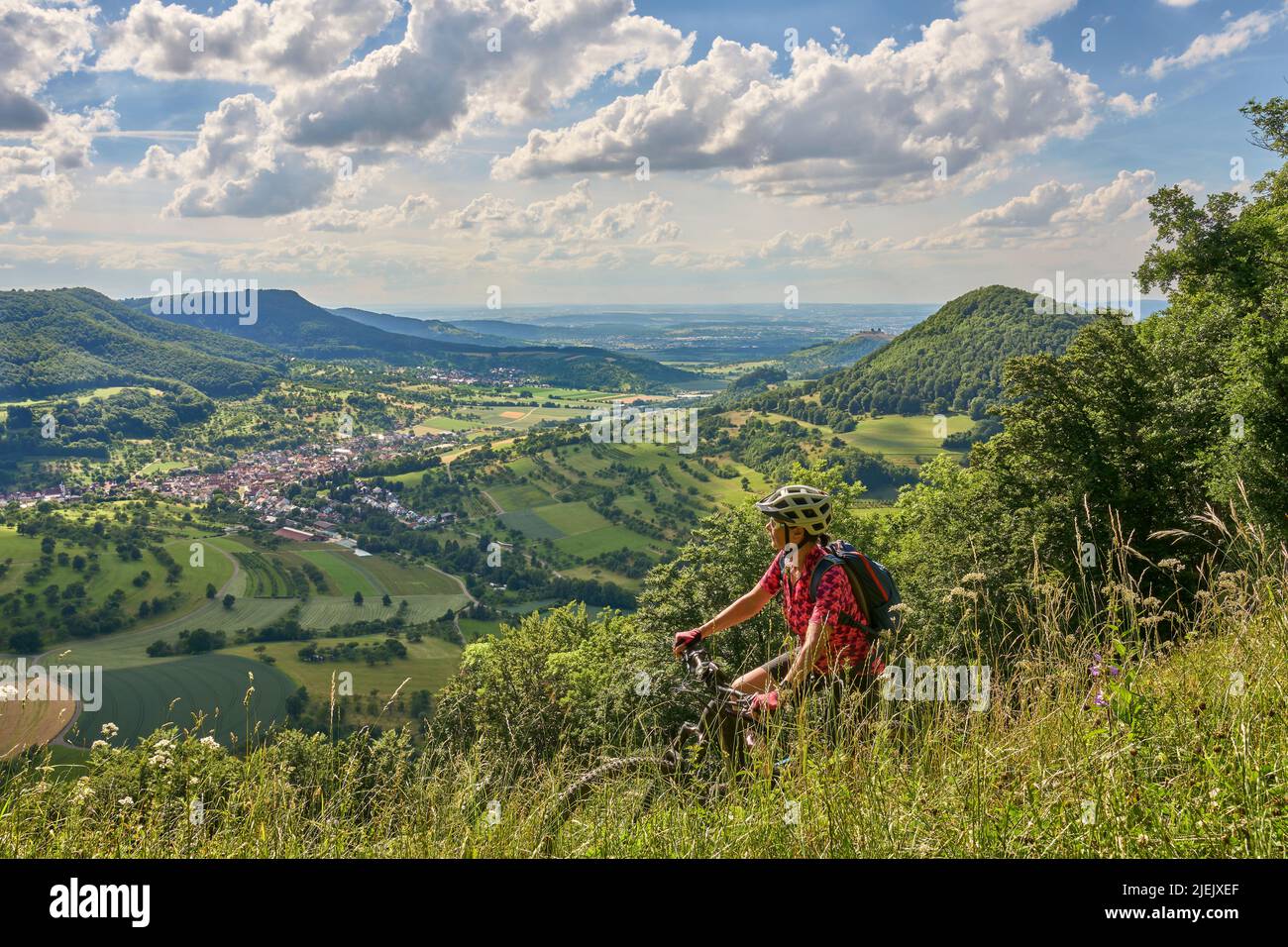 Nette ältere Frau, die mit ihrem Elektro-Mountainbike an einem Aussichtspunkt auf der Schwäbischen Alb über dem Dorf Neidlingen, Baden-Württemberg, unterwegs ist Stockfoto