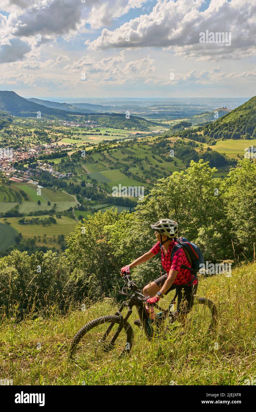 Nette ältere Frau, die mit ihrem Elektro-Mountainbike an einem Aussichtspunkt auf der Schwäbischen Alb über dem Dorf Neidlingen, Baden-Württemberg, unterwegs ist Stockfoto