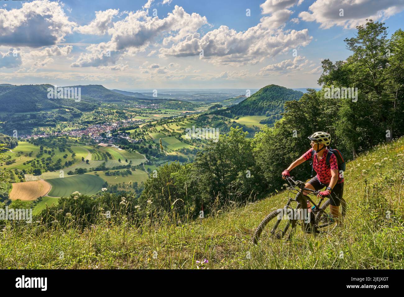 Nette ältere Frau, die mit ihrem Elektro-Mountainbike an einem Aussichtspunkt auf der Schwäbischen Alb über dem Dorf Neidlingen, Baden-Württemberg, unterwegs ist Stockfoto