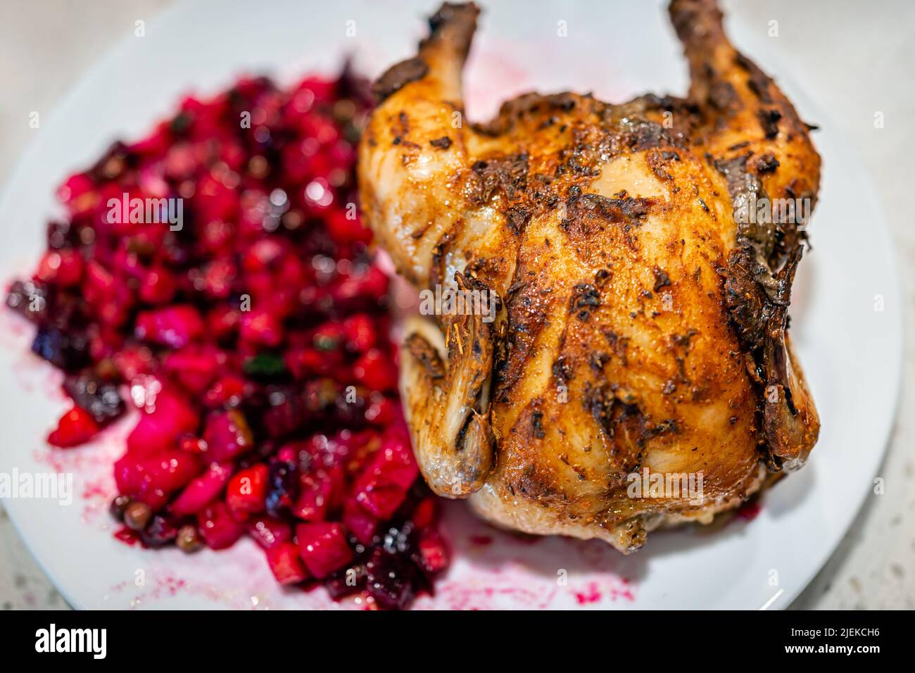 Makro-Nahaufnahme von russischem oder ukrainischem gekochtem Rübenkartoffelsalat namens Vinaigrette auf dem Teller mit einer ganzen gerösteten kornischen Henne und knuspriger Haut Stockfoto