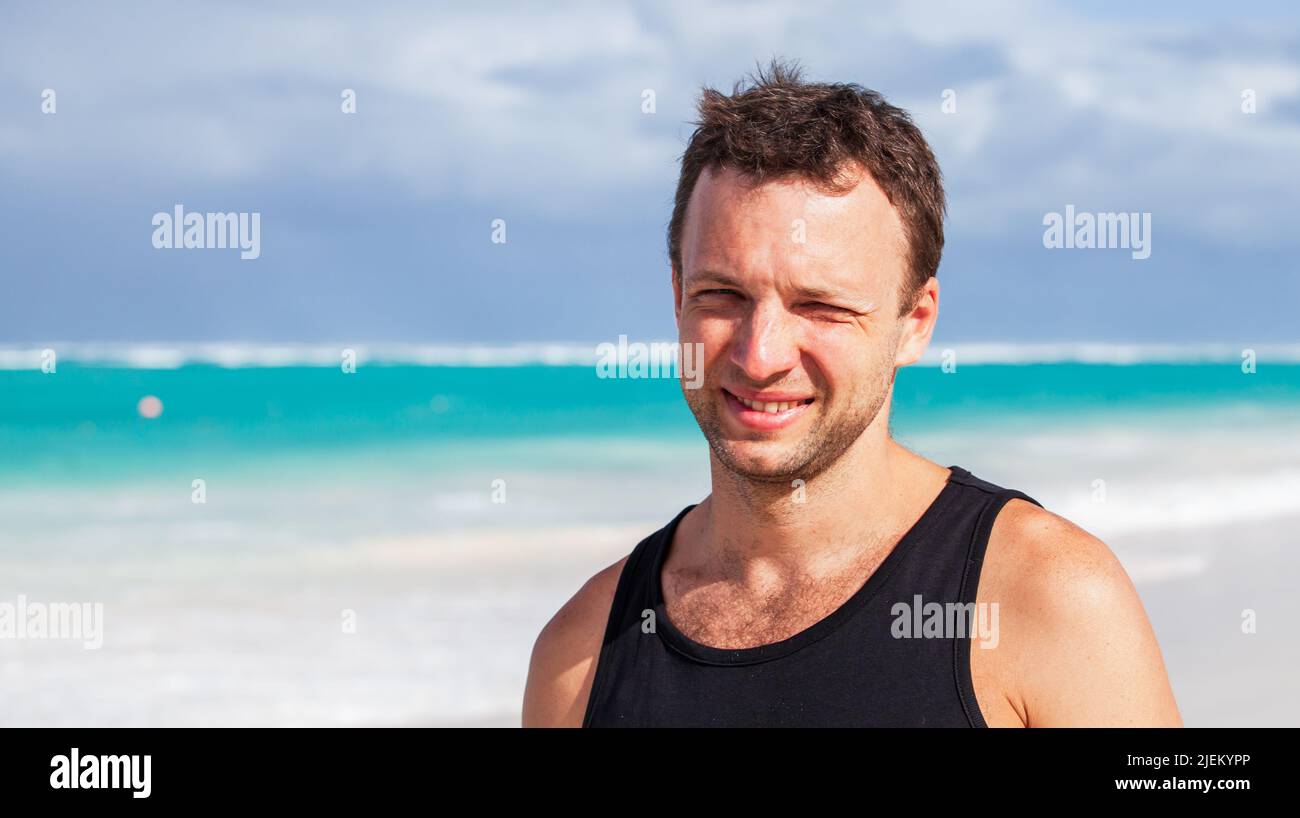 Porträt eines lächelnden jungen erwachsenen kaukasischen Mannes in schwarzem Hemd, der an einem sonnigen Sommertag am Strand in der Dominikanischen Republik steht Stockfoto