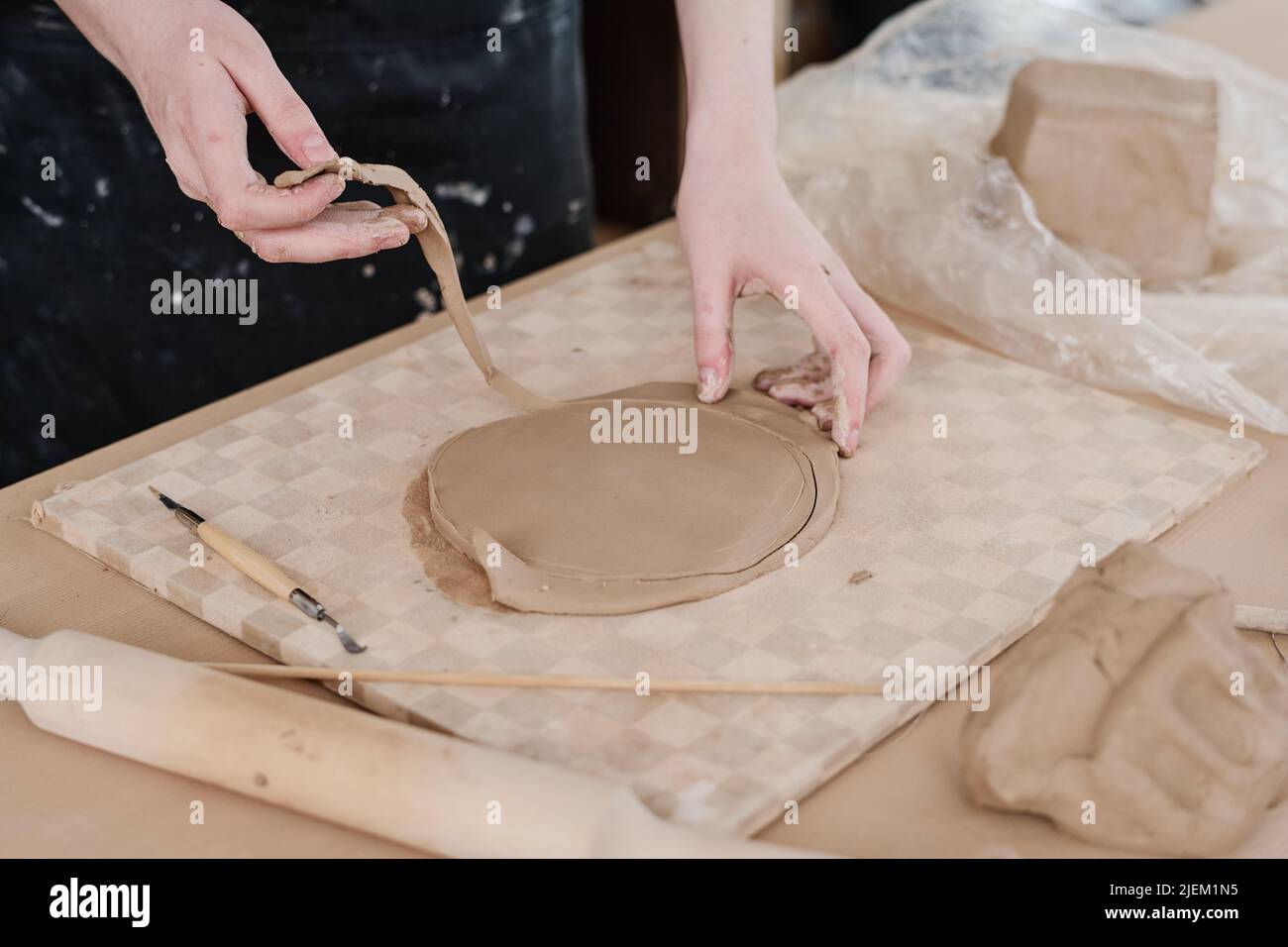 Hände von jungen Handwerker in Schürze wegnehmen übermäßige Ton, um genaue runde Form des Werkstücks für kreative eaarthenware Artikel zu erhalten Stockfoto