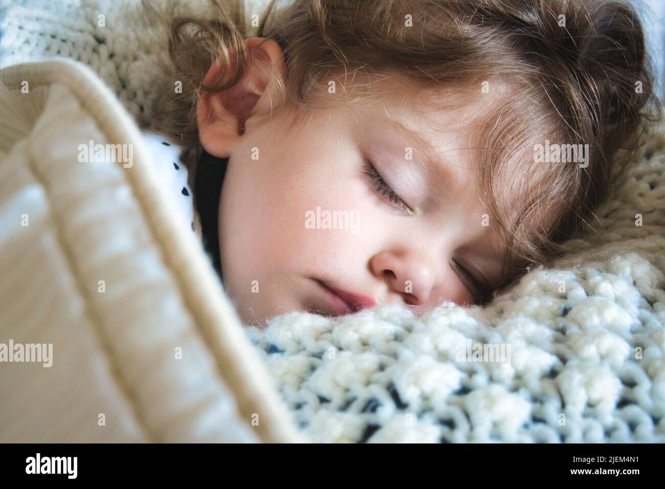 Nahaufnahme eines kleinen Mädchens, das friedlich in eine warme Decke gehüllt schläft Stockfoto