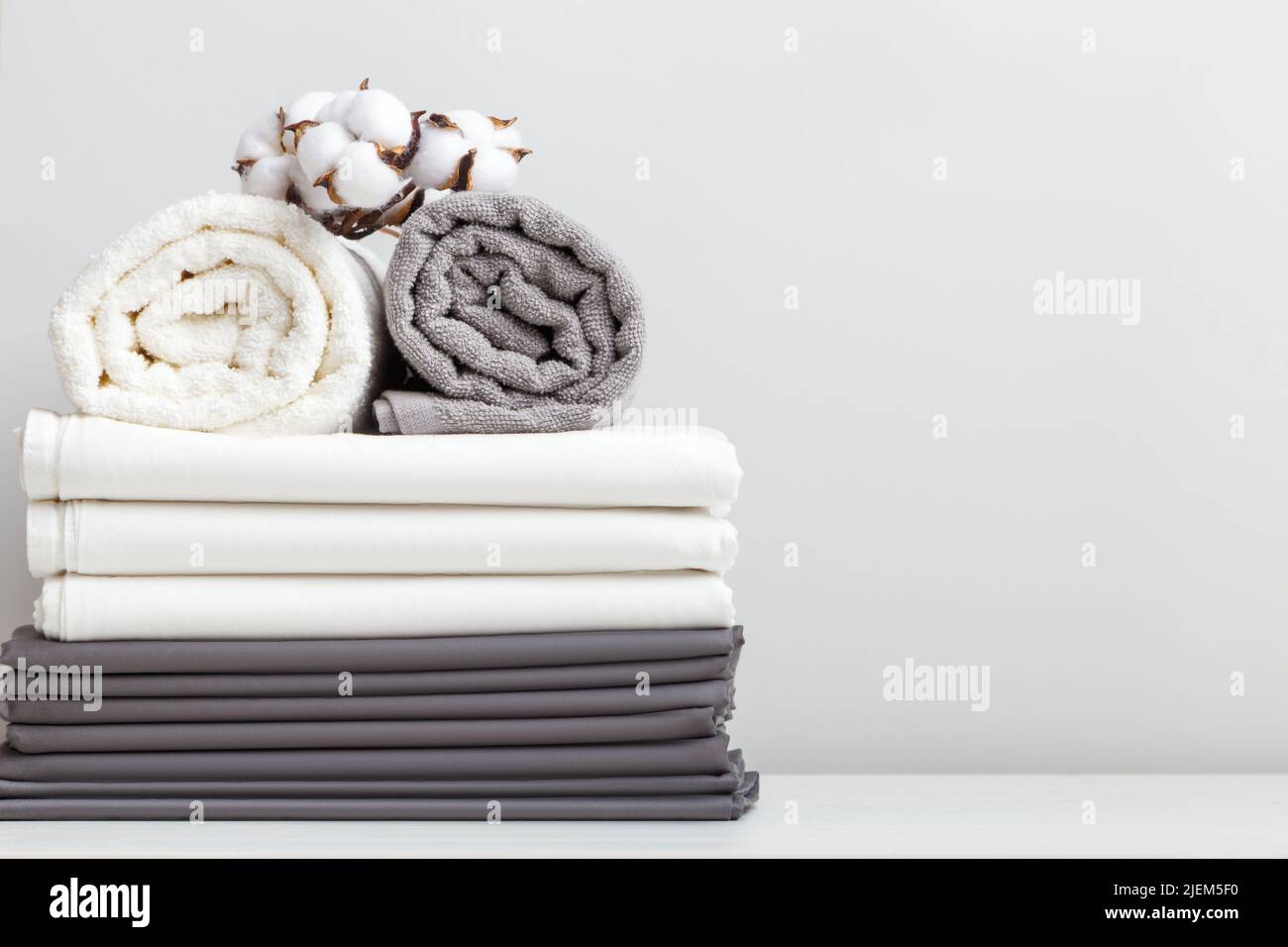 Grauweiße Bettwäsche, ein Laken und zwei zusammengerollte Handtücher auf dem Tisch. Stockfoto