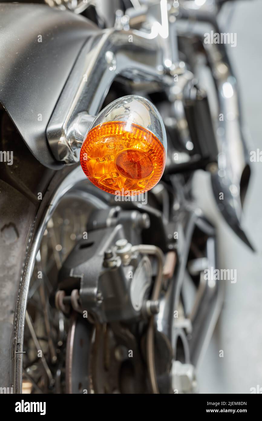 Ein orangefarbenes Blinklicht, ein Signal und eine Anzeige auf einem glänzend schwarzen Motorrad. Nahaufnahme Detaillierte Textur der Warnlampe zur Verkehrssicherheit, Vorsichtsmaßnahme Stockfoto