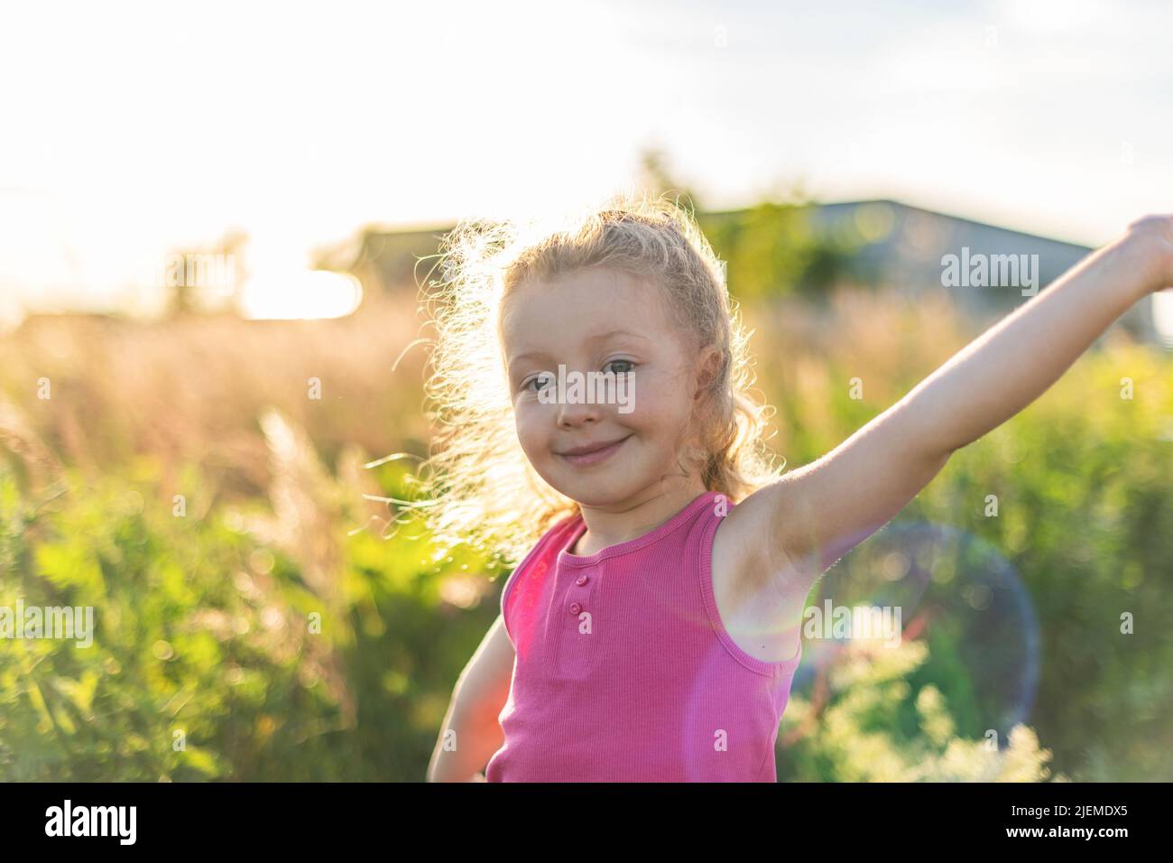 Kleine fröhliche blonde Mädchen vor dem Hintergrund von Gras und Sonnenuntergang Stockfoto