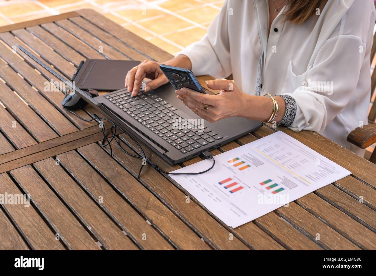 Frau, die von zu Hause aus im Garten mit Laptop und Mobiltelefon Telearbeit angestellt hat. Stockfoto