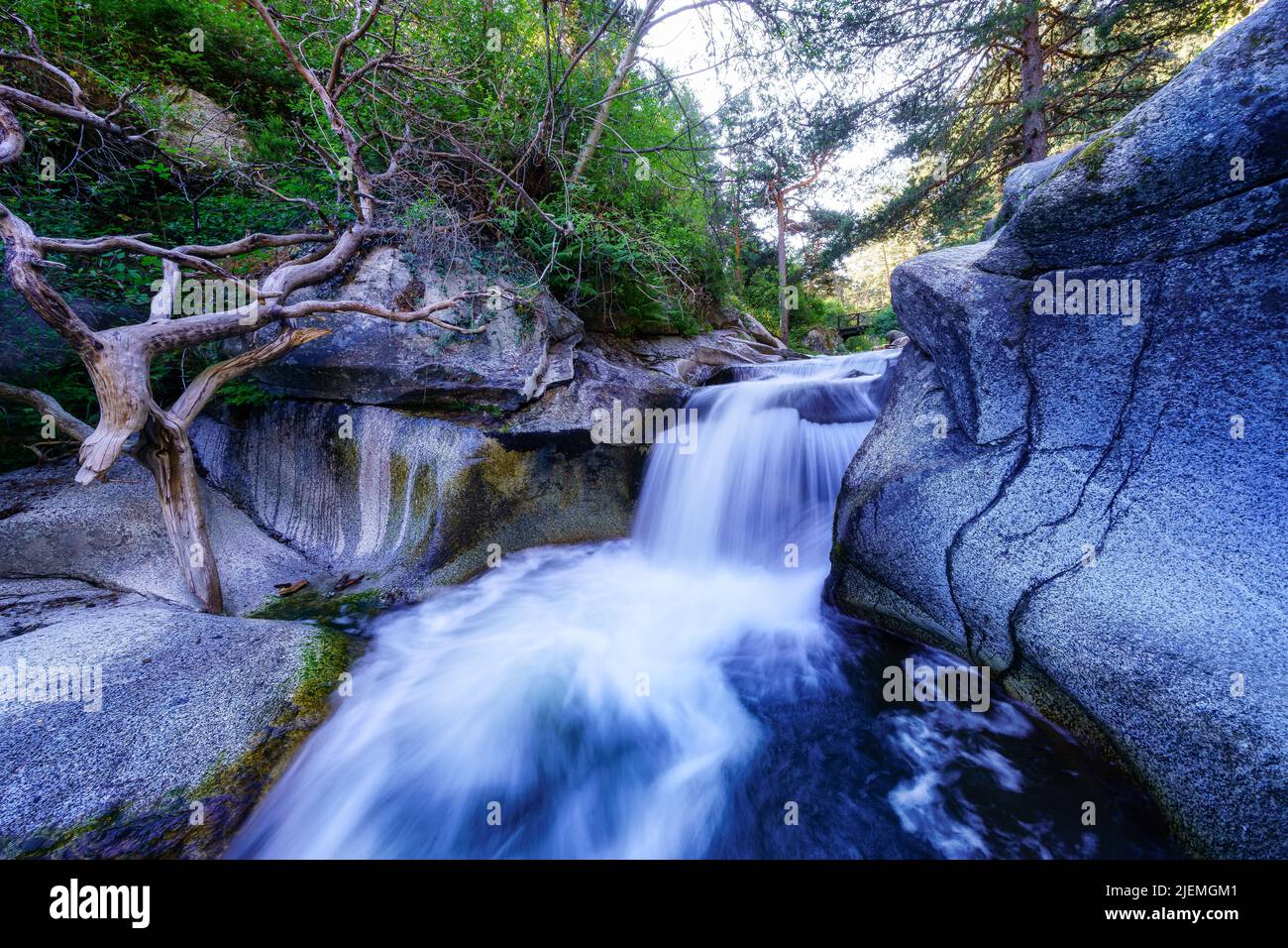 Wasserfall am Fluss zwischen Felsen und grüner Vegetation bei Sonnenaufgang. Navacerrada. Stockfoto