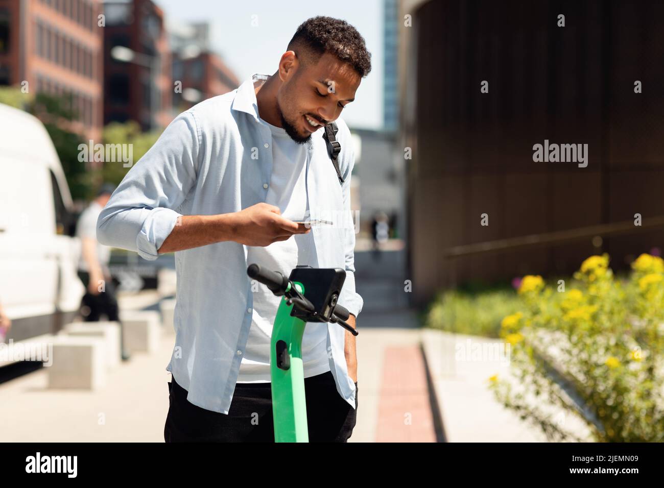 Elektroroller-Sharing-Services. Junger Schwarzer, der in der Stadt E-Scooter ausmietet und online mit dem Smartphone bezahlt Stockfoto
