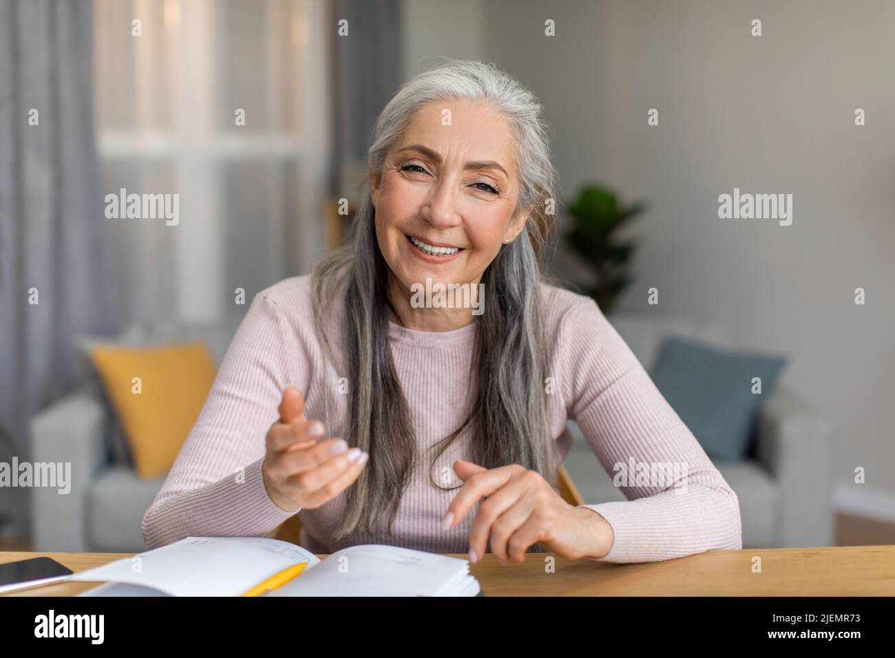 Fröhlich lächelnd europäische reife Lehrerin mit grauen Haaren treffen sich und schaut in die Kamera im Wohnzimmer Stockfoto