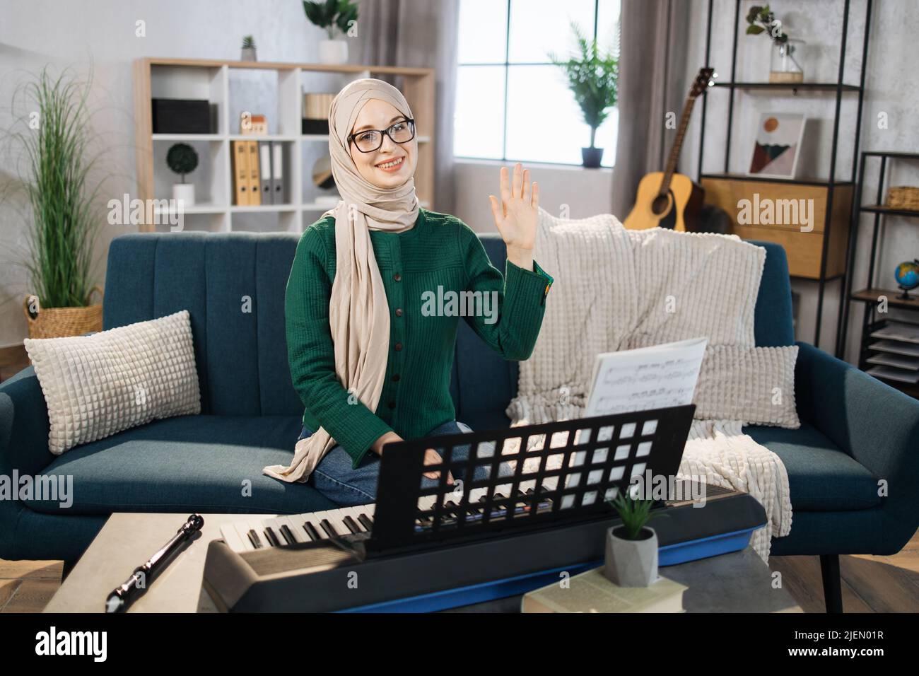 Portrait eines muslimischen Mädchens in Hijab, das Klavier spielt. Hübsche Frauen in der Musiktherapie, indem sie Klavier im Musikzimmer spielen. Junge arabische weibliche Mädchen im Klavierunterricht. Entspannen zu Hause mit der Hand winken. Musikkonzept. Stockfoto