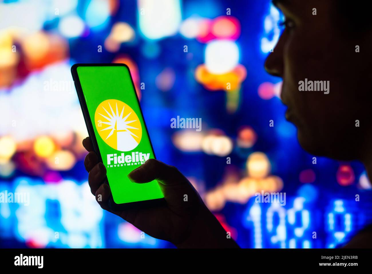 In dieser Abbildung hält eine silhouettierte Frau ein Smartphone mit dem Fidelity Investments-Logo auf dem Bildschirm. Stockfoto