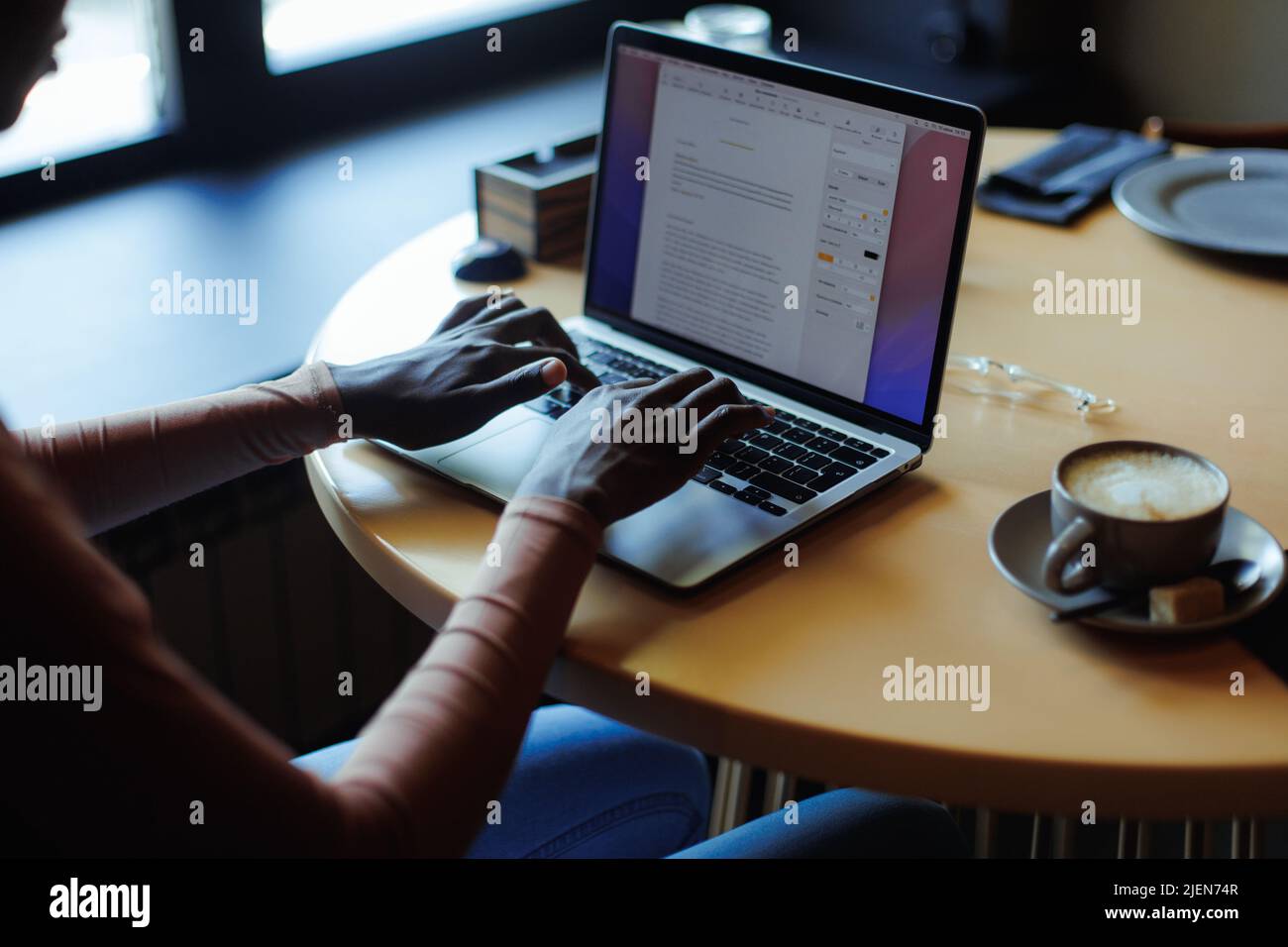 Zugeschnittenes Foto einer afroamerikanischen Frau, die am beigefarbenen Holztisch sitzt und mit einem grauen Laptop beim Tippen arbeitet. Technologie. Stockfoto