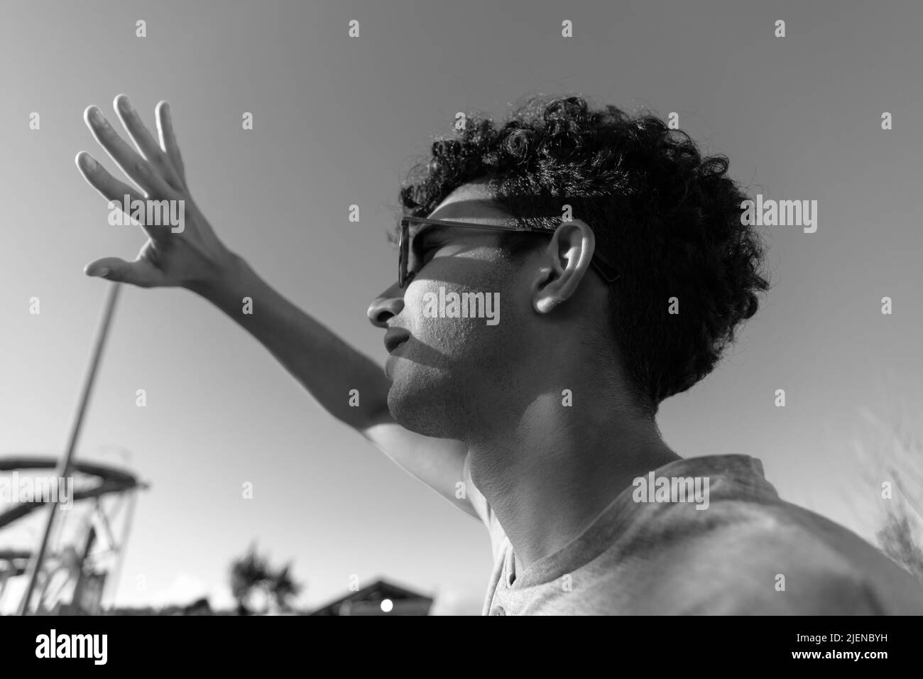 Junger lateiner in einem Vergnügungspark, der die Sonne anschaut und seine Hand bedeckt, was Schatten auf seinem Gesicht verursacht. Stockfoto