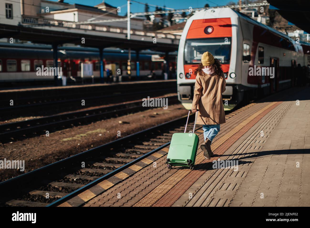 Glückliche junge Reisende Frau mit Gepäck, das im Zug am Bahnsteig des Bahnhofs an Bord geht. Rückansicht. Stockfoto