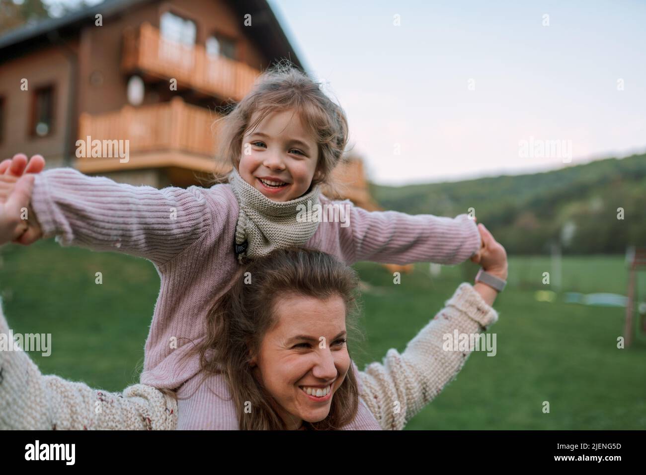 Glückliche Mutter mit kleiner Tochter auf Huckepack laufen und Spaß zusammen im Garten in der Nähe ihres Hauses. Stockfoto