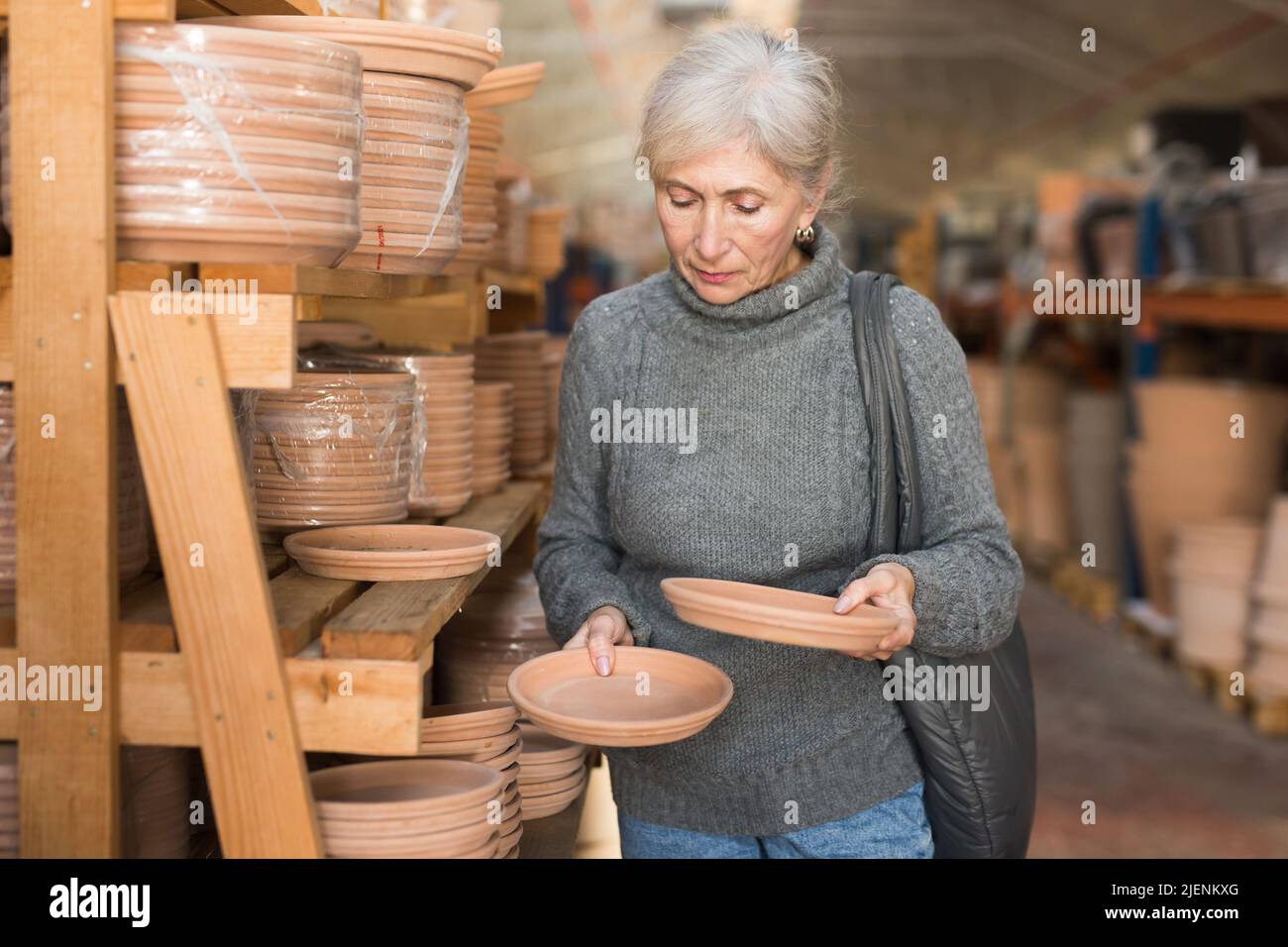 Ältere Frau auf der Suche nach Töpfen für den Anbau von Pflanzen im Gewächshaus Stockfoto